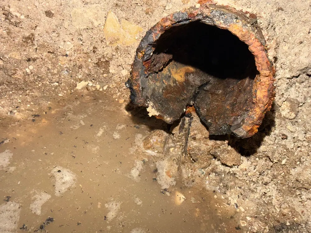 Rusted-through cast-iron drain pipe found during a dig, broken open in wet soil