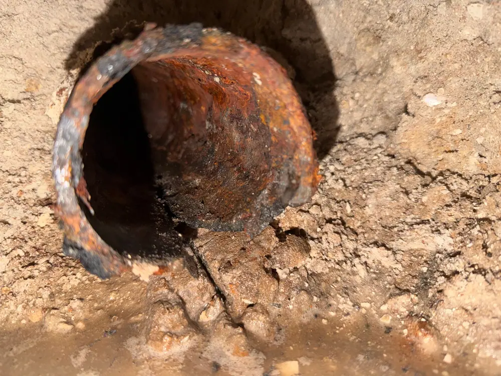 Open end of a corroded cast-iron drain line in a trench before replacement