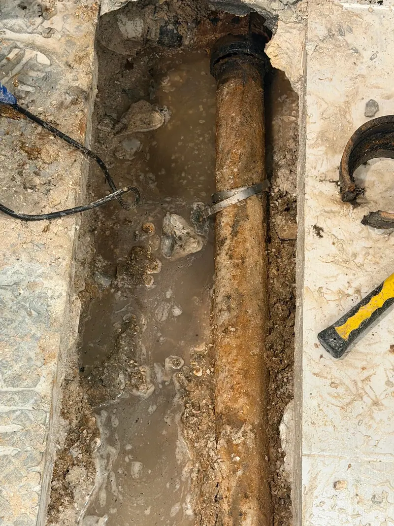 Trench cut through a slab floor exposing rusted cast-iron drain pipe