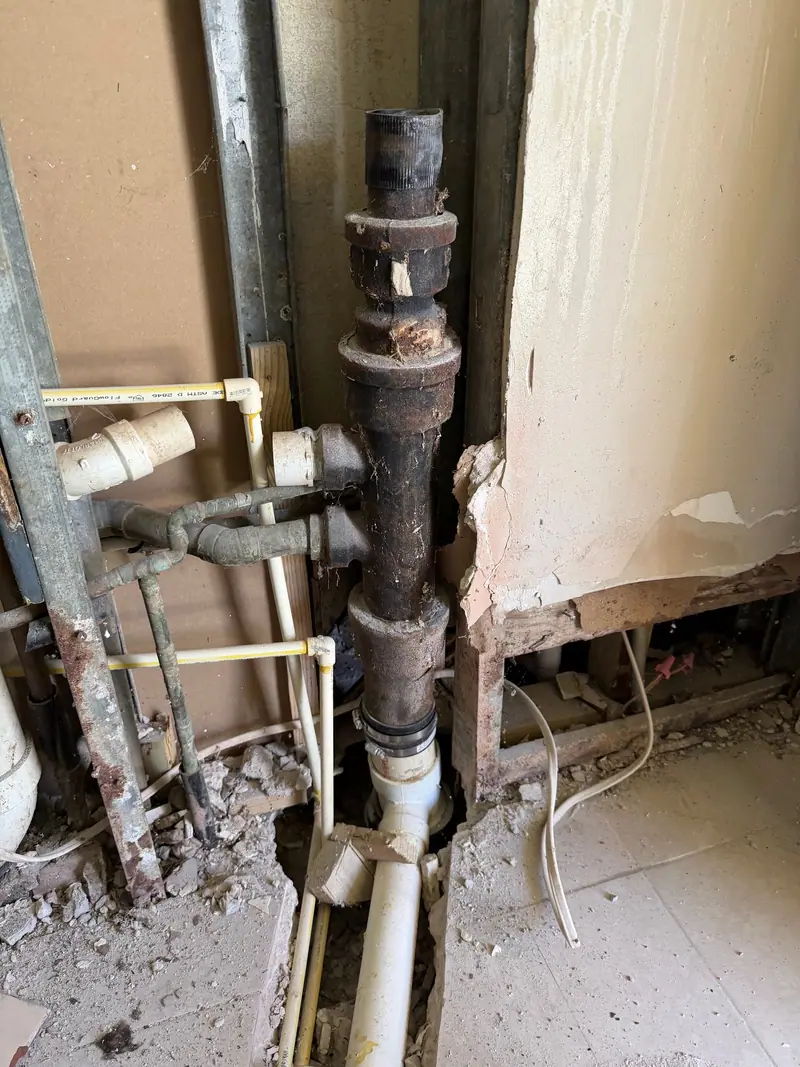 Cast-iron drain stack tied into new white PVC inside a wall