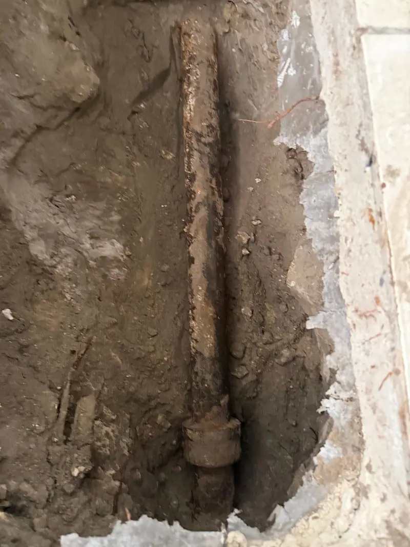 Corroded cast-iron drain and fitting exposed in a slab trench