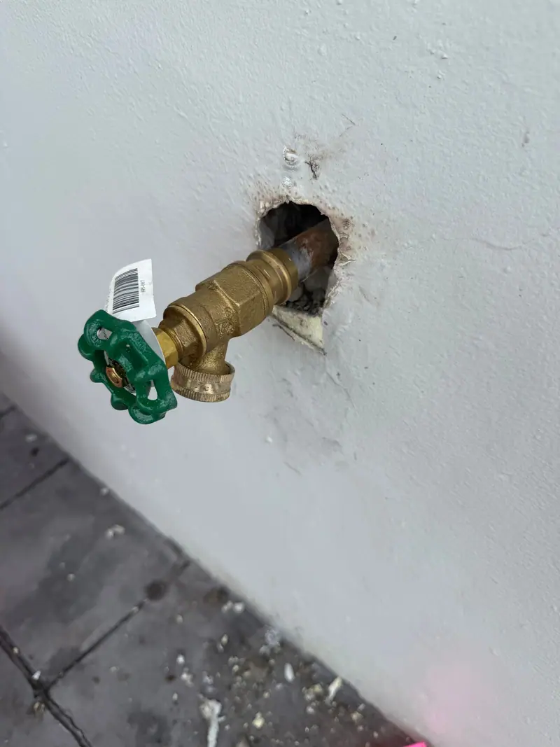 New brass hose bib with a green handle on a stucco wall