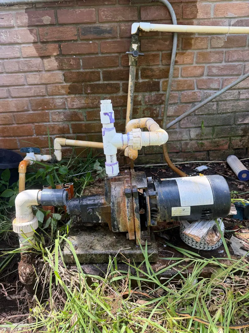 Sprinkler pump motor with a PVC tee against a brick wall