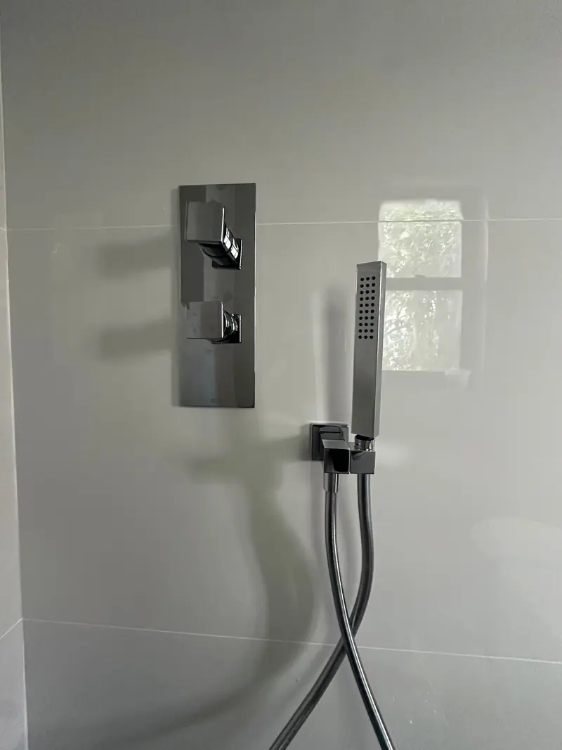 Finished shower wall with valve trim and a handheld shower