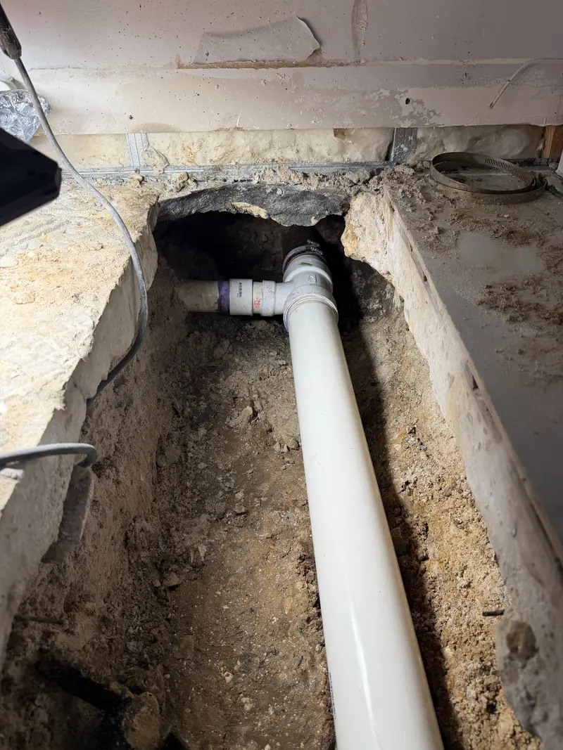 New white PVC drain line laid into a trench cut through a slab floor
