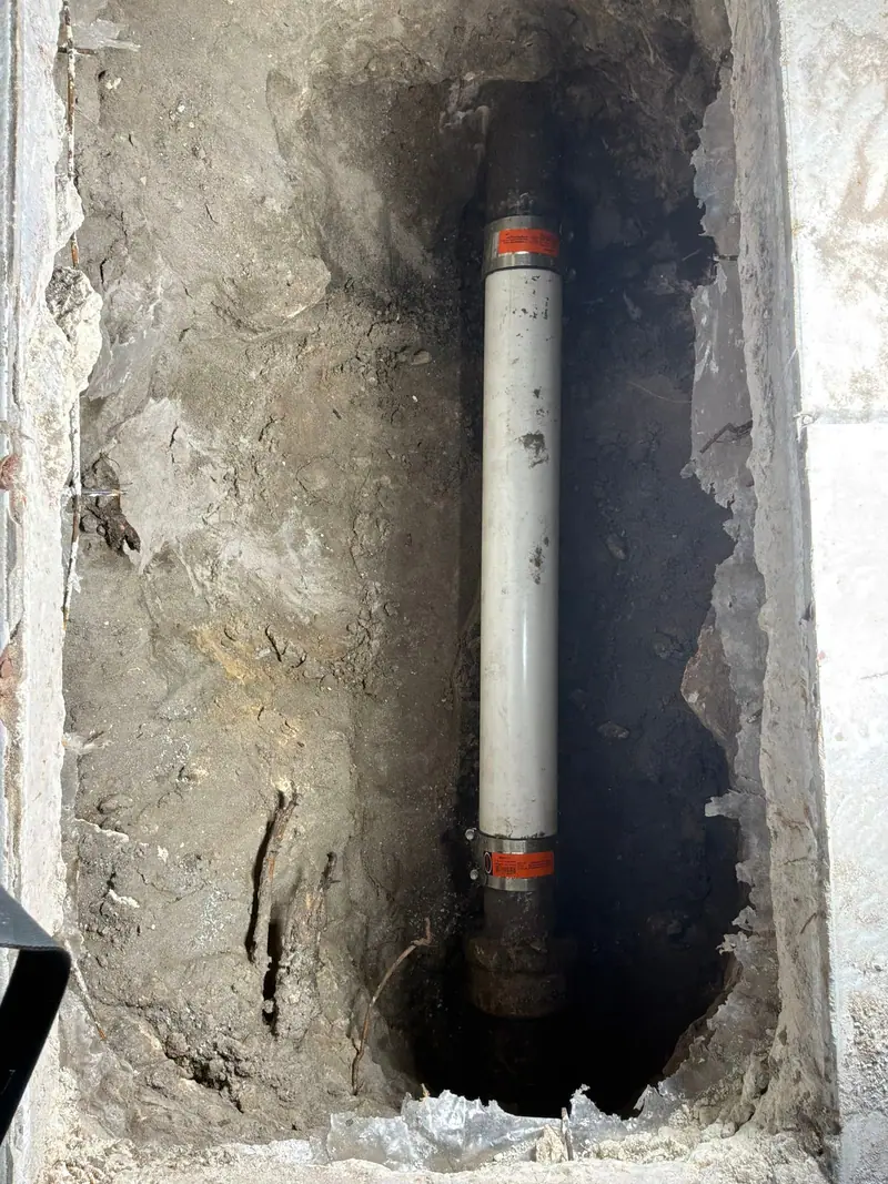 Narrow trench in a concrete slab with a new white PVC drain riser