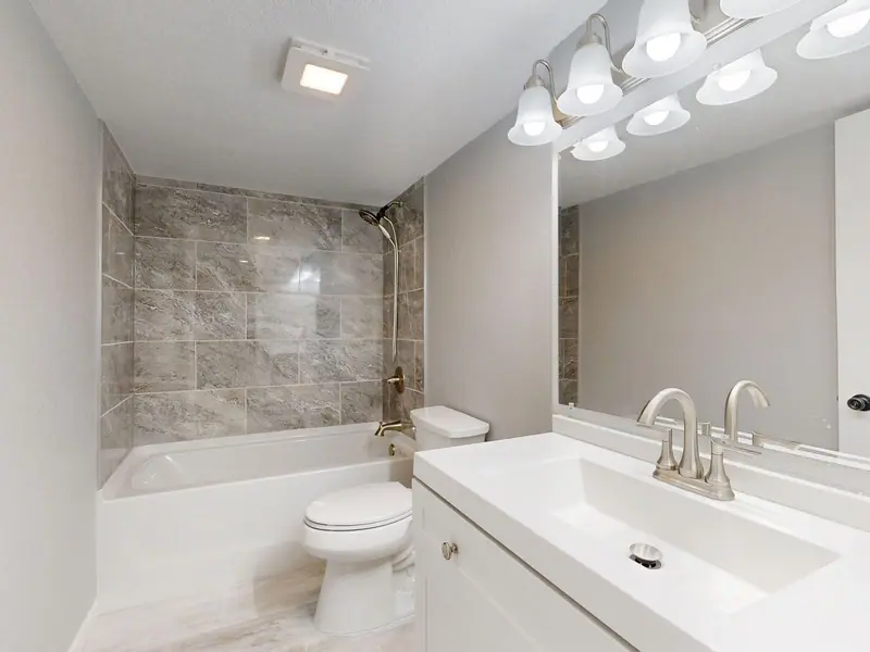 A bright bathroom with a white vanity, chrome faucet and tub surround
