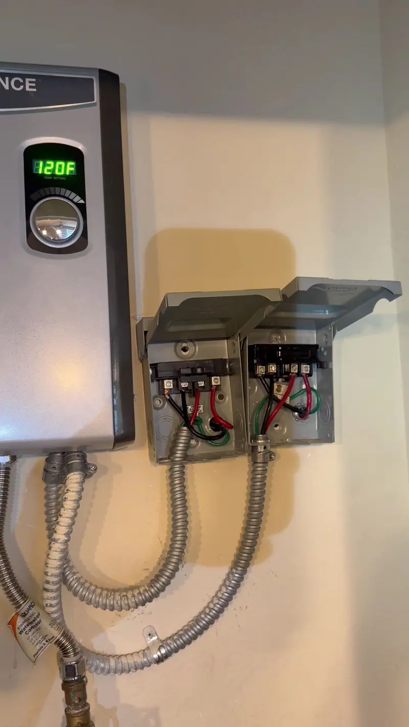 Electric tankless water heater on a wall with its disconnect boxes