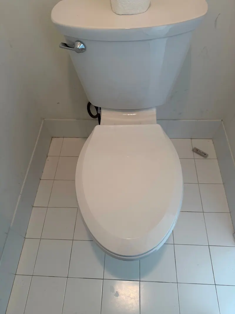 New white toilet installed in a small white-tile bathroom
