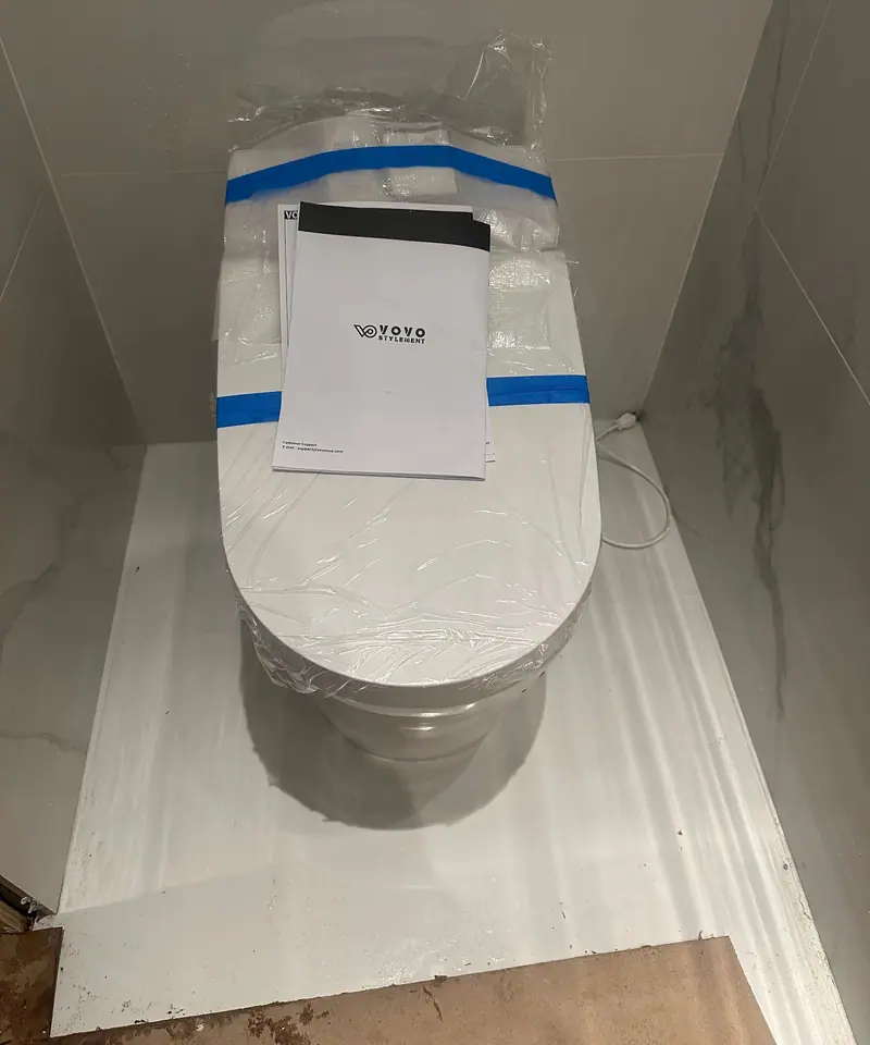 New wall-hung toilet just installed, still taped, in a marble niche