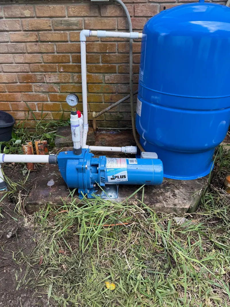 Blue well jet pump and pressure tank with new PVC piping beside a brick wall