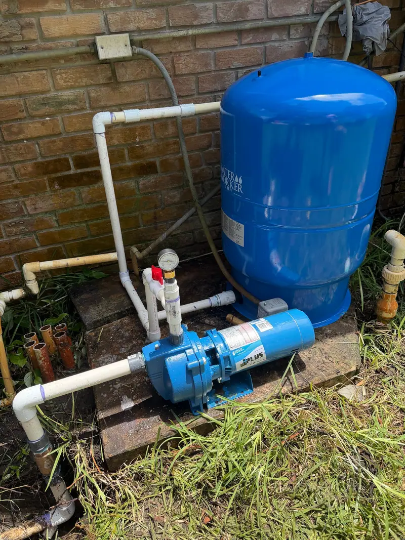 Pressure tank and jet pump set on a pallet beside a brick house, piped in PVC