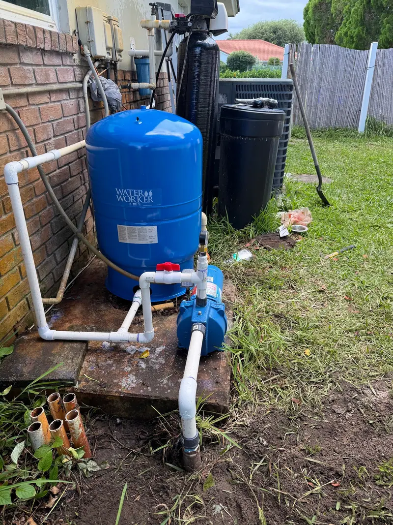 Pressure tank and pump plumbed along the side of a brick house