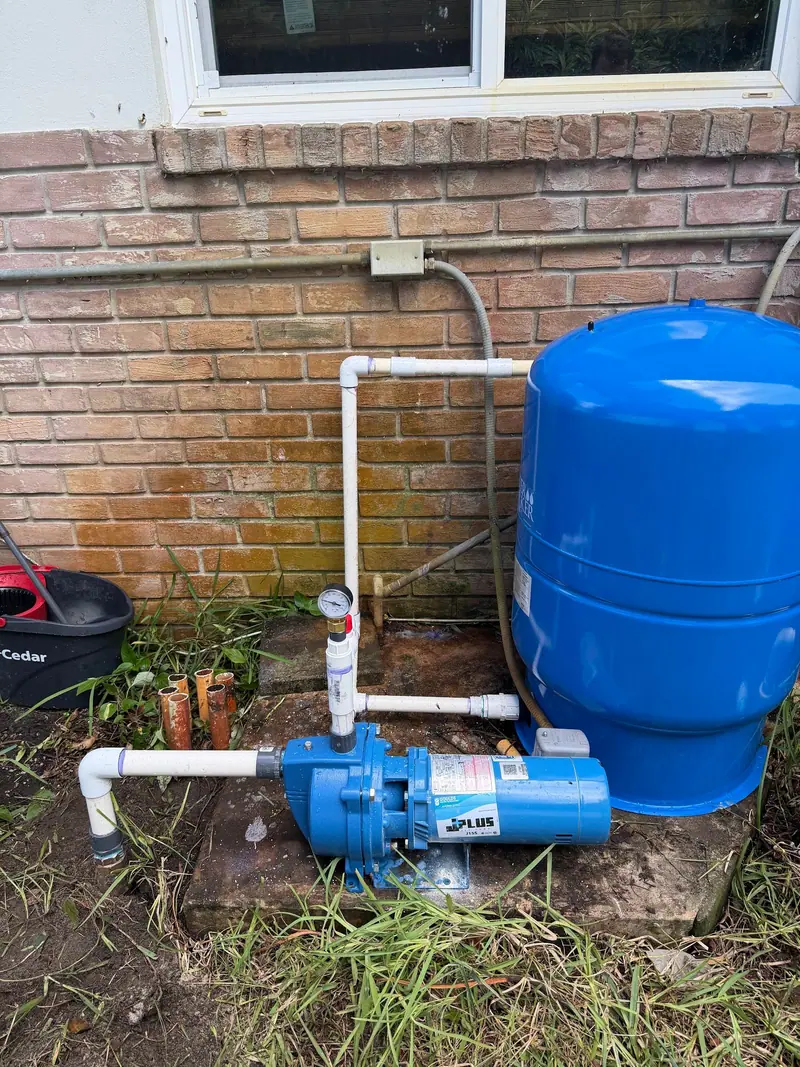 Blue pressure tank and well pump piped in PVC below a window
