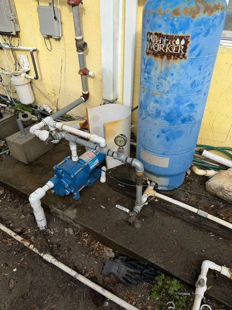 Well system with pressure tank, pump and PVC manifold against a yellow wall