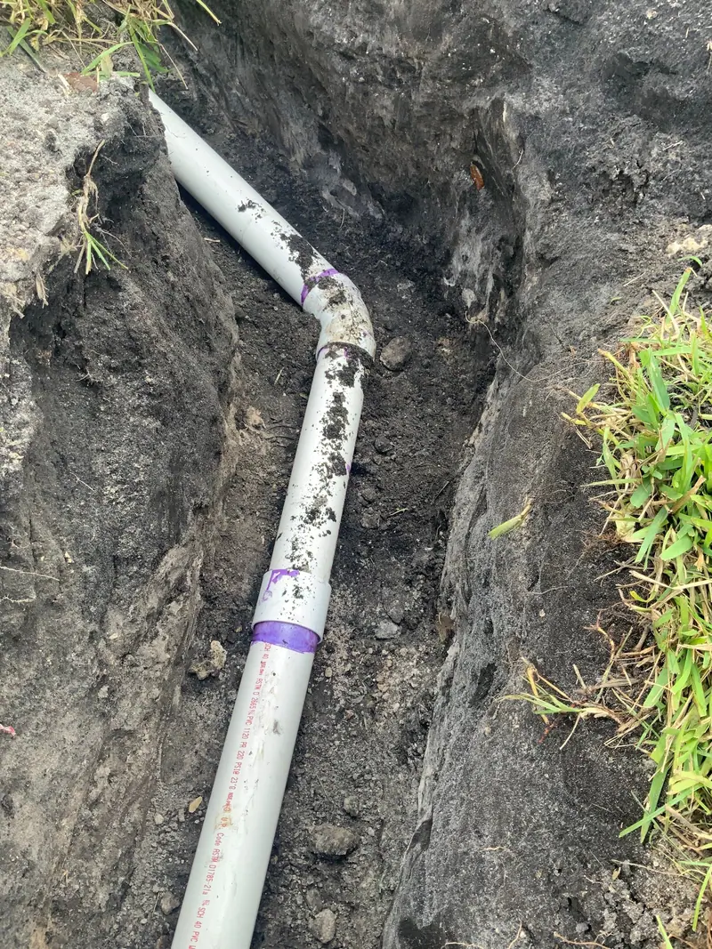 New white PVC line with a purple primer band turning through a yard trench